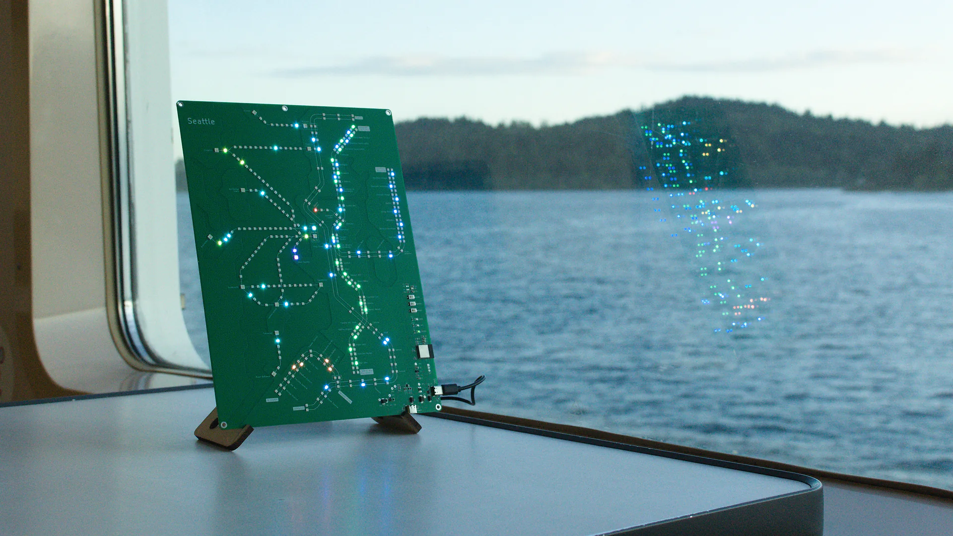 Seattle Transit Live illuminated beside a ferry window on Puget Sound